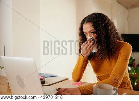 Multi-cultural Young Adult Female Blowing Her Nose While Working From Home On Her Laptop. Modern Apa