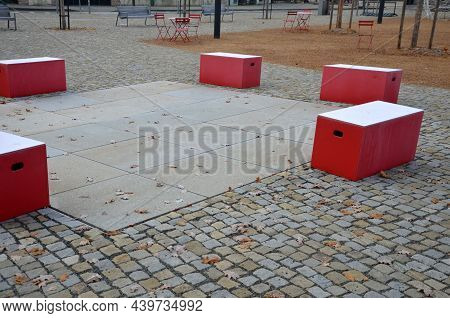 Red Plastic Benches In The Shape Of Blocks With Handles. The Square Is Paved With Granite Cubes. San
