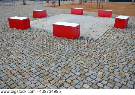 Red Plastic Benches In The Shape Of Blocks With Handles. The Square Is Paved With Granite Cubes. San