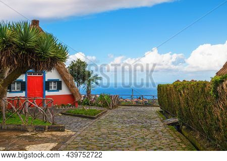Traditional House With Atlantic Ocean In The Background In The Village Of Santana On Madeira Island,