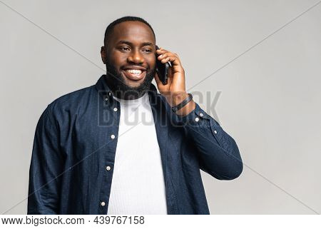 Overjoyed African-american Guy Talking On The Smartphone Over Grey Background. Multiracial Man Enjoi