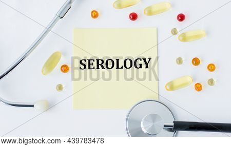 The Word Serology On A Yellow Card On A White Background Next To Scattered Pills And A Stetscope