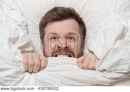 Caucasian Man Is Under Stress, Suffers From Insomnia, Cannot Sleep, Nervously Bites The Blanket And 