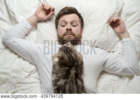 Man In White Pajamas Was Awakened By Beloved Cat, Who Lay Sleeping On Chest, He Looks At Her Sleepil