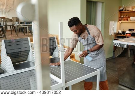 Young African American Man Wearing Apron Starting Workday In Modern Cafe Preparing Tables For Custom
