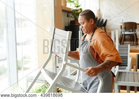 Side View Shot Of Stylish Young Woman Working In Modern Cafe Placing Chairs And Tables Before Openin