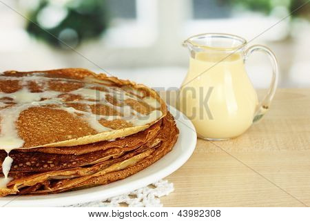 หวาน pancakes บนแผ่นกับนมข้นบนโต๊ะในห้องครัว