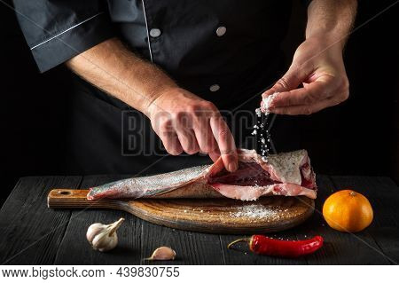 Professional Chef Prepares Fresh Fish Sprinkling Salt. Preparing To Cook Fish Food. Working Environm