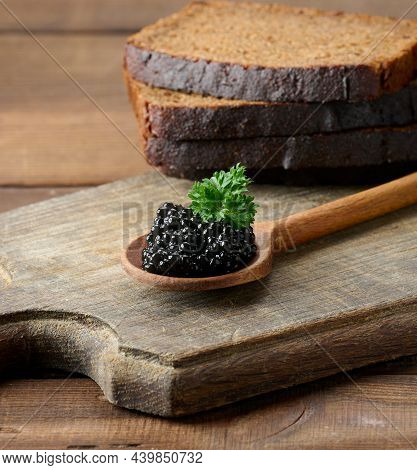 Fresh Grainy Black Paddlefish Caviar In Brown Wooden Spoon On A Brown Table, Close Up