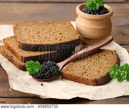 Fresh Grainy Black Paddlefish Caviar In Brown Wooden Spoon On A Brown Table, Close Up