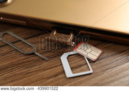 Sim Card, Mobile Phone And Ejector Tool On Wooden Table, Closeup