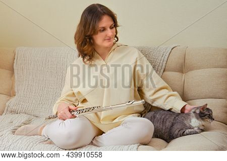 A Woman With A Flute Is Playing At Home On The Sofa In The Living Room