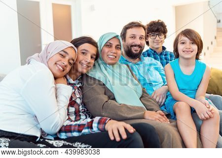 Portrait photo of an arab muslim family sitting on a couch in the living room of a large modern house. Selective focus 