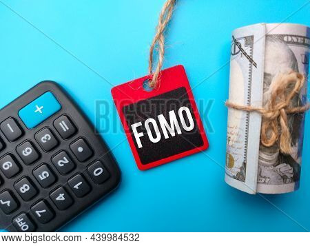 Calculator,banknotes And Colored Wooden Board With Text Fomo On Blue Background.