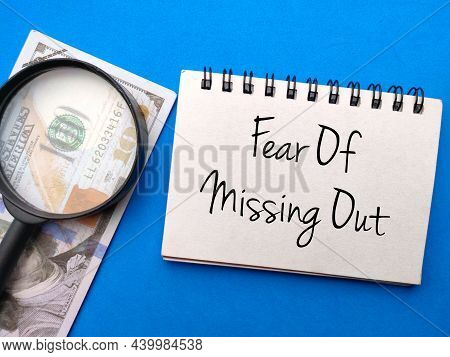 Banknotes,mangnifying Glass And Notebook With Text Fear Of Missing Out On Blue Background.