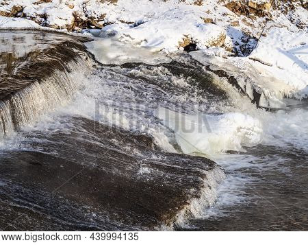 A Stream Of Water Flows Among Ice And Snow. Dark Cascade Stream Of Water Among White Snow And Ice