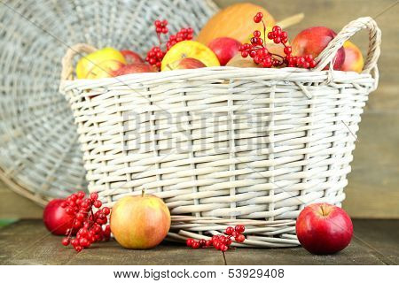 Juicy apples and pumpkin in wooden basket on table close-up