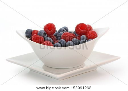 raspberries and blueberries in bowl isolated on white background