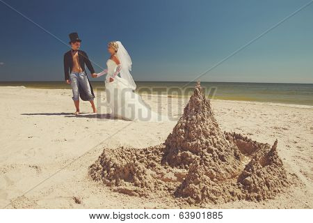 A young and beautiful newly-married couple enjoying on the beach near sandy castle at the sea edge