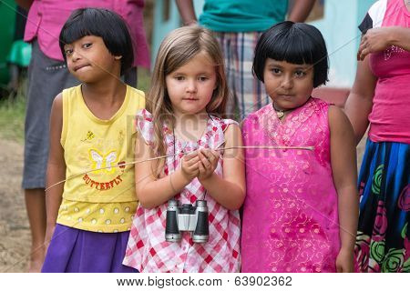 ELLA, SRI LANKA - MARCH 2, 2014: Little blonde girl posing with two local girls. Ella is famous for the tea plantations and stunning views across the countryside.