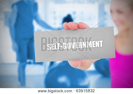 Fit blonde holding card saying self govenment against trainer and client in fitness studio