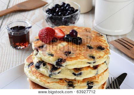 Blueberry Pancake Closeup with syrup pitcher, wooden spatula and fork, blueberry bowl and other items set out for a homemade breakfast. Horizontal format.