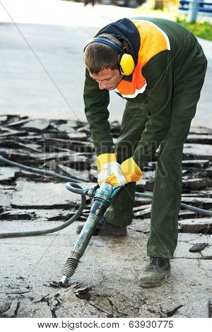 Builder worker with pneumatic jack hammer drill equipment breaking asphalt at construction road works