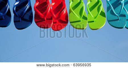 Blue, red, green and turquoise flipflops hanging with a sky background