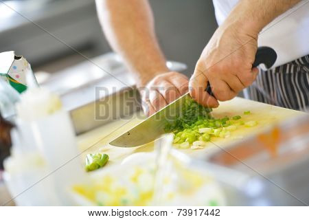 Handsome chef dressed in white uniform decorating pasta salad and seafood fish in modern kitchen
