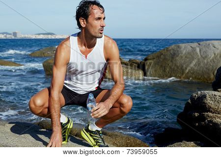 Male fit runner resting while sitting on rocks on the beach