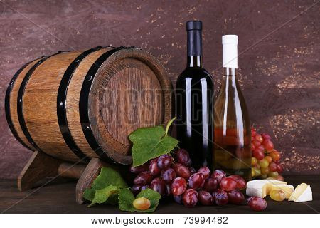 Wine in bottles, Camembert and brie cheese, grapes and wooden barrel on wooden table on wooden background
