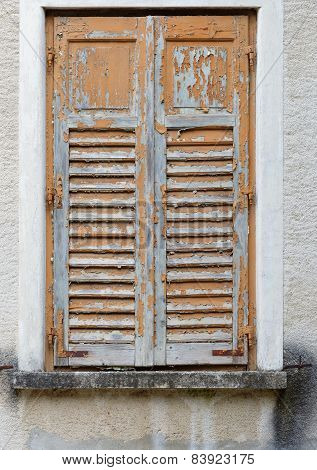 Closed old window covered by wooden blinds with peeling paint
