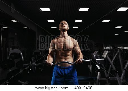 Muscular man working out in gym doing exercises with barbell at biceps, strong male naked torso abs. Muscular bodybuilder doing exercise with barbell. Bodybuilder in the gym