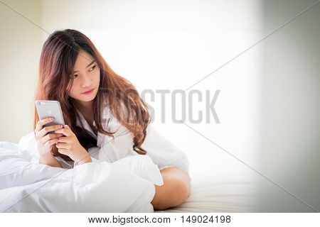 Girl Using A Mobile Phone Lying On The Bed At Home