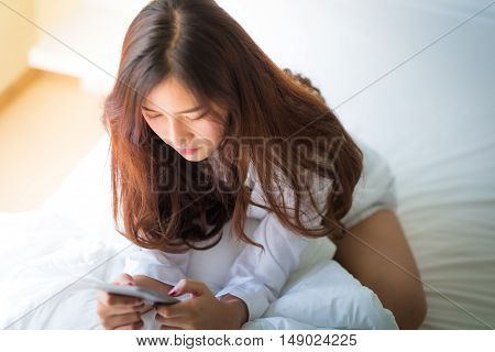 Girl Using A Mobile Phone Lying On The Bed At Home