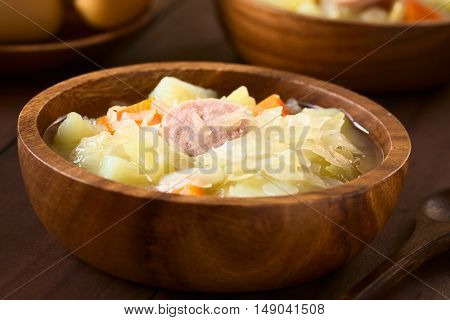 Sauerkraut soup or stew prepared with potato carrot and bratwurst served in wooden bowl photographed with natural light (Selective Focus Focus in the middle of the dish)