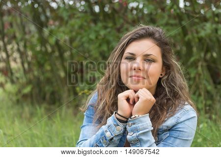 Portrait of brunette teenage girl sitting outdoors. Girl is supporting her chin by fists
