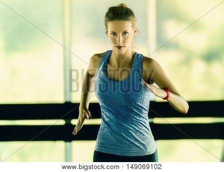 Energetic runnning workout of a young woman in a glass framed corridor. She wears a fitness tracker on her left arm.