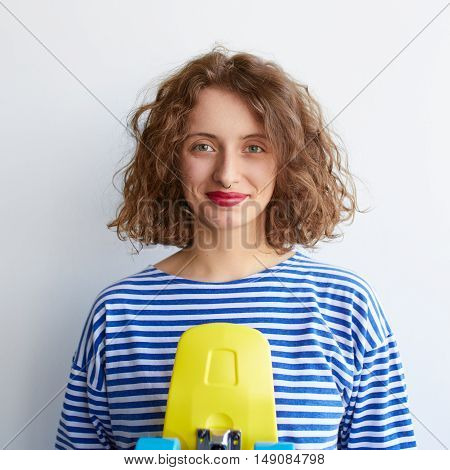 Hipster girl holding a yellow color skateboard over white background. Curly cute young woman with pennyboard