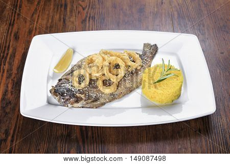 on the table a plate of grilled fish trout with lemon fried onion rings with sesame seeds and as a garnish rice and rosemary.