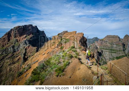 Woman hiker with green backpack doing her hike of Pico Arieiro to Pico Ruivo hiking route. Madeira island popular hike, Portugal.