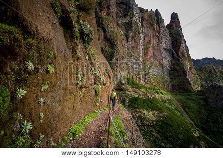 Woman hiker is going on the edge of steep mountain at Madeira island. Pico Arieiro hiking path.