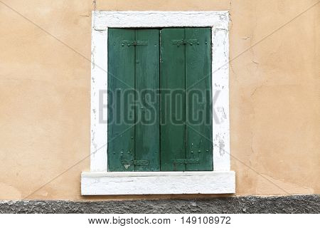Old window with closed shutters with flowers on the window sill on the stone wall. Italian Village.