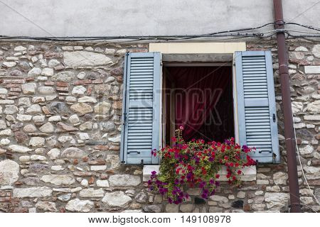 Old window with open shutters with flowers on the window sill on the stone wall. Italian Village.