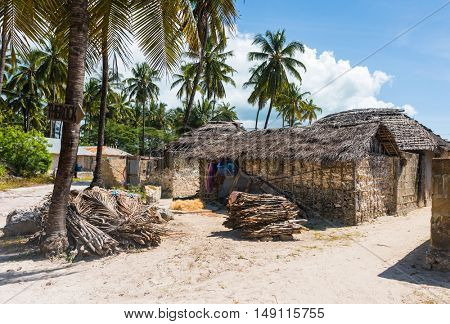 houses with thatch roofs and bundles of firewood on african beach with palms, Zanzibar