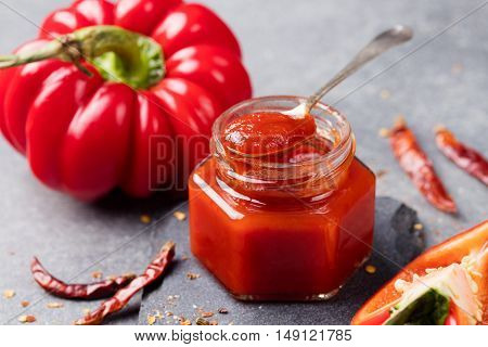 Tomato and chili sauce, jam confiture in a glass jar on a grey stone background