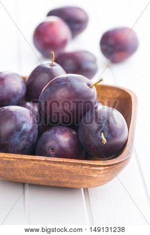 Fresh ripe plums in wooden bowl on white table.