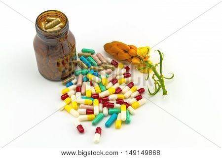 Colorful tablets medicine in black bottle and fresh flower of Senna alata isolate on white background