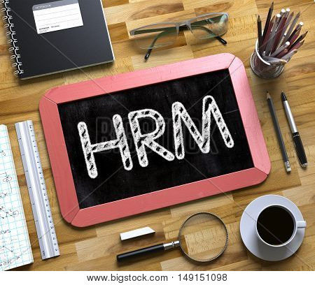 Small Chalkboard with HRM Concept. Business Concept - HRM Handwritten on Red Small Chalkboard. Top View Composition with Chalkboard and Office Supplies on Office Desk. 3d Rendering.