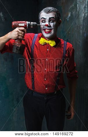 The scary clown and electric drill on dack. Halloween concept of horror and murderer